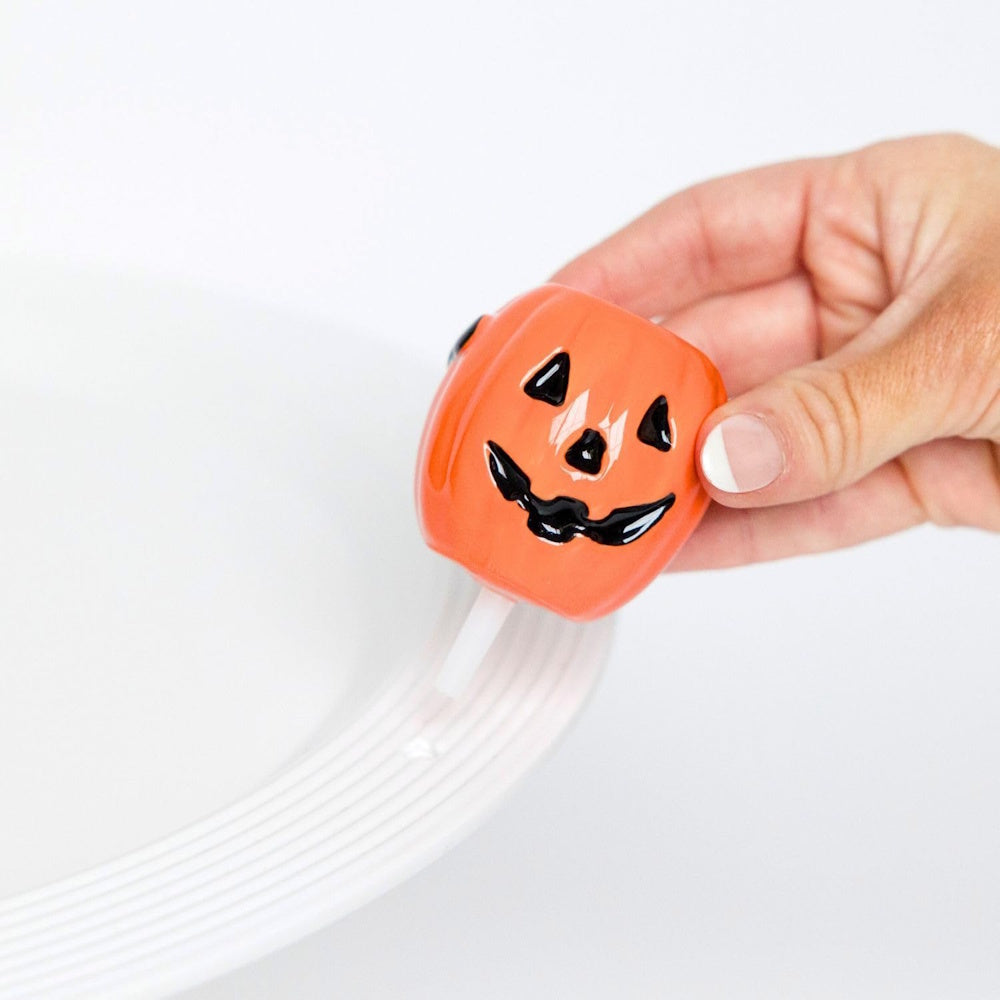 A hand placing a small, ceramic jack-o'-lantern platter decoration into the rim of a white plate.