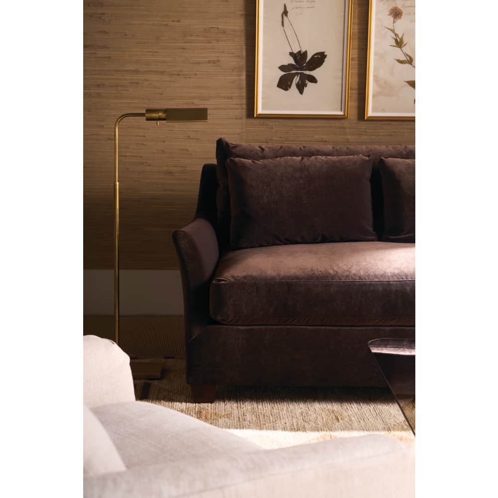 Brown velvet Moreau sofa next to a gold floor lamp in a warm, textured living room.