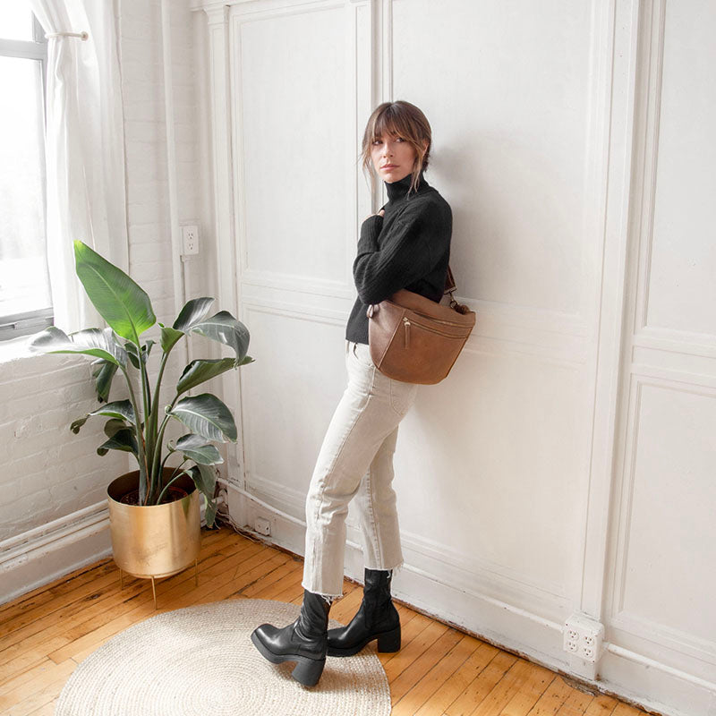 Woman wearing russet brown and olive leather large sling crossbody bags with gold zippers.