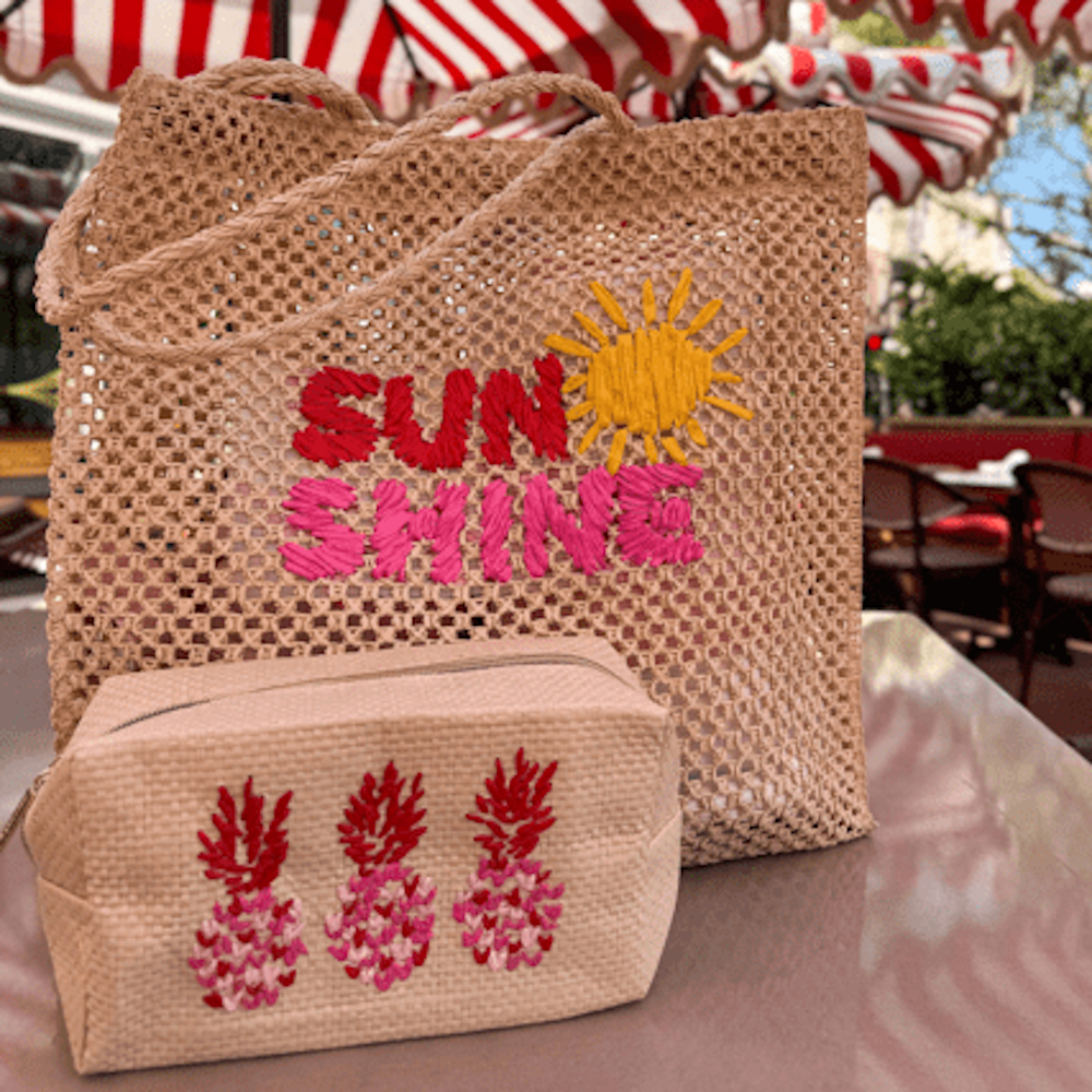 Woven beige tote bag with embroidered "SUNSHINE" and sun icon, next to a matching pineapple-embroidered pouch.