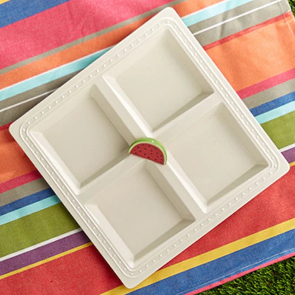 Square white four-compartment serving platter with a central watermelon slice accent, on a striped cloth.