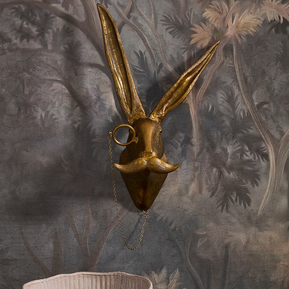 A golden hare head wall mount with long ears, a monocle on a chain, and a prominent mustache.