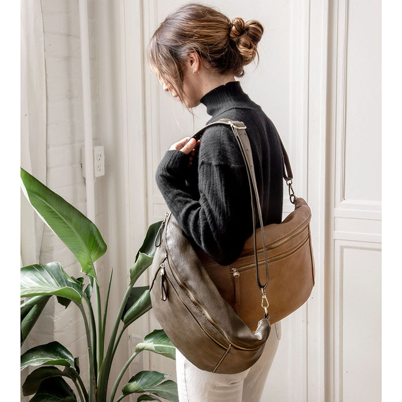 Woman wearing a black turtleneck and white pants, carrying a large olive green and a tan leather sling crossbody bag.
