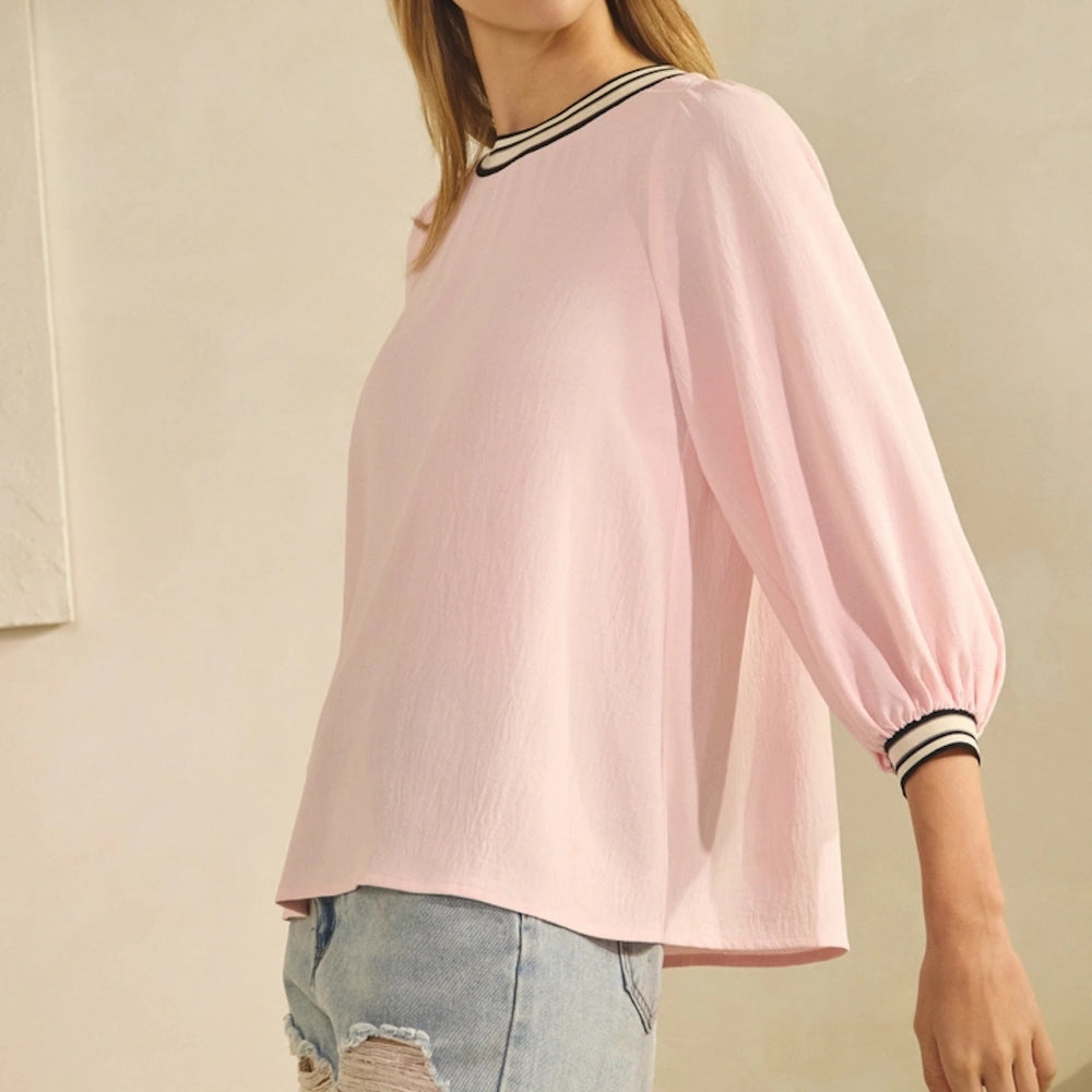 Light blush pink airflow top with striped trim on the neckline and cuffs, paired with distressed denim jeans.
