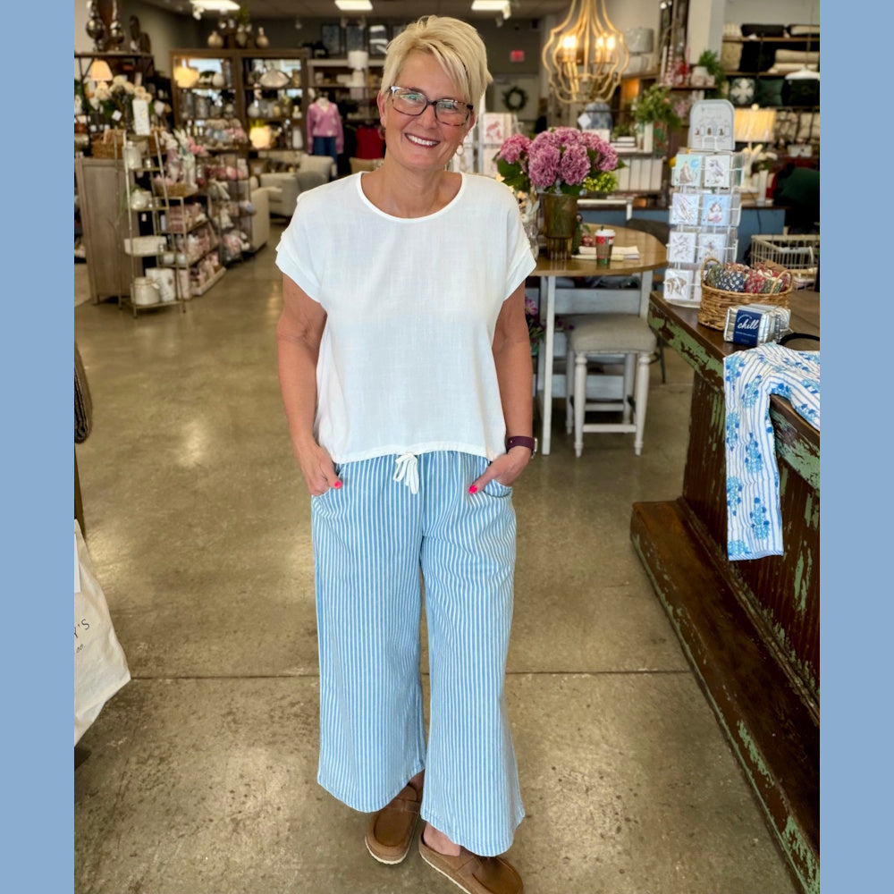 Woman in a white short-sleeve top and light blue vertical striped wide-leg denim pants standing in a boutique.