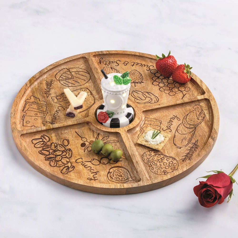Round wooden charcuterie tray with four sections and a central light-up ceramic drink sitter on a marble surface.