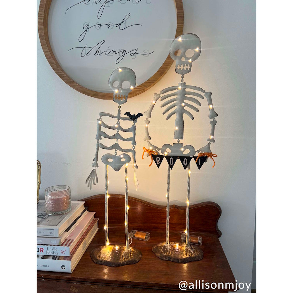 Two light-up Halloween skeleton decorations with fairy lights on a wooden tabletop display.