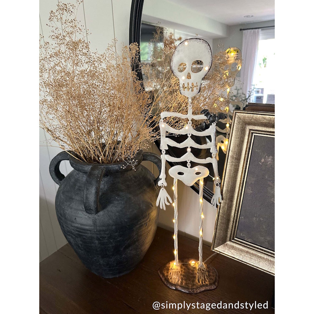Light-up metal skeleton Halloween decoration next to a black rustic vase with dried grass.