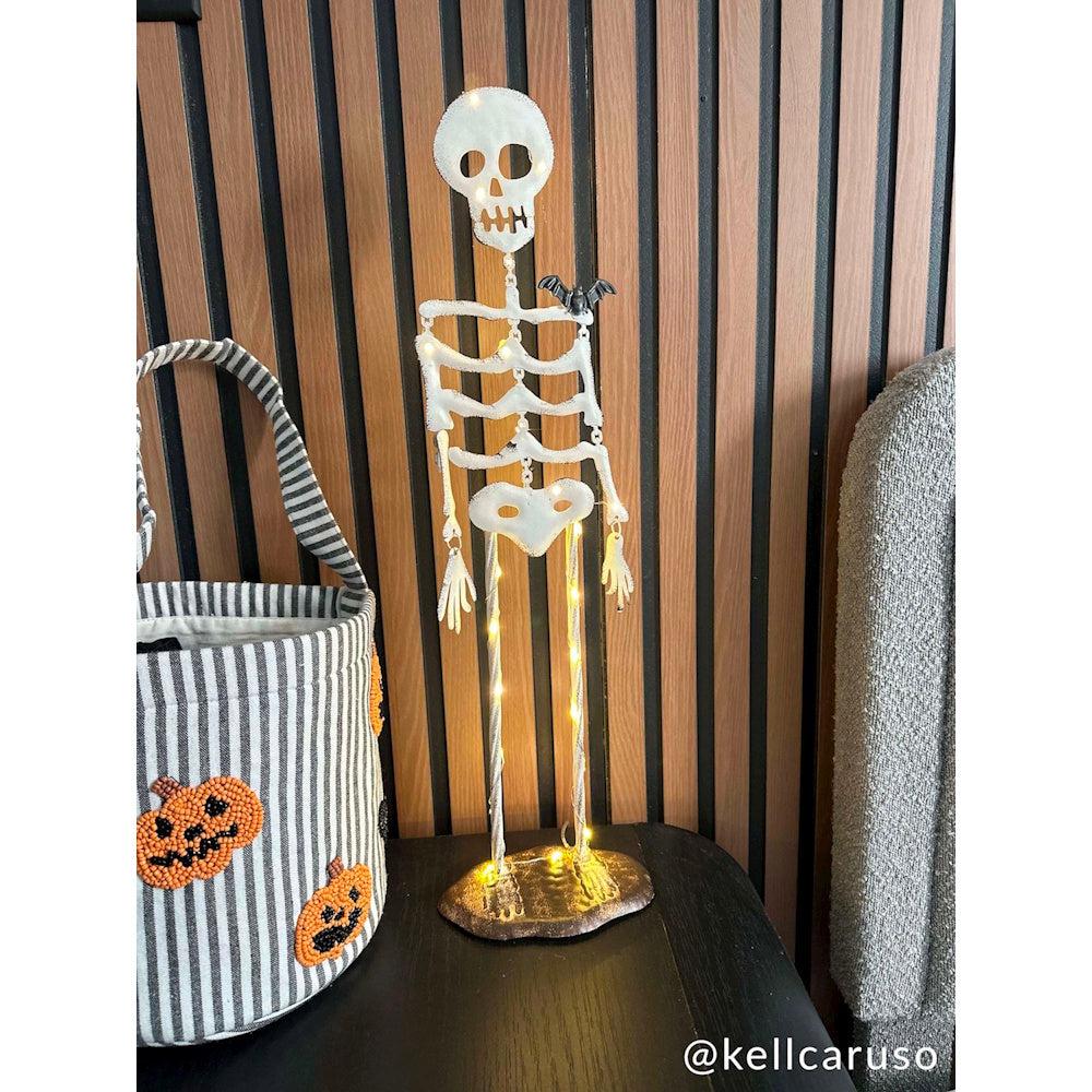 Light-up standing Halloween skeleton figurine with bat detail next to a striped pumpkin tote bag.