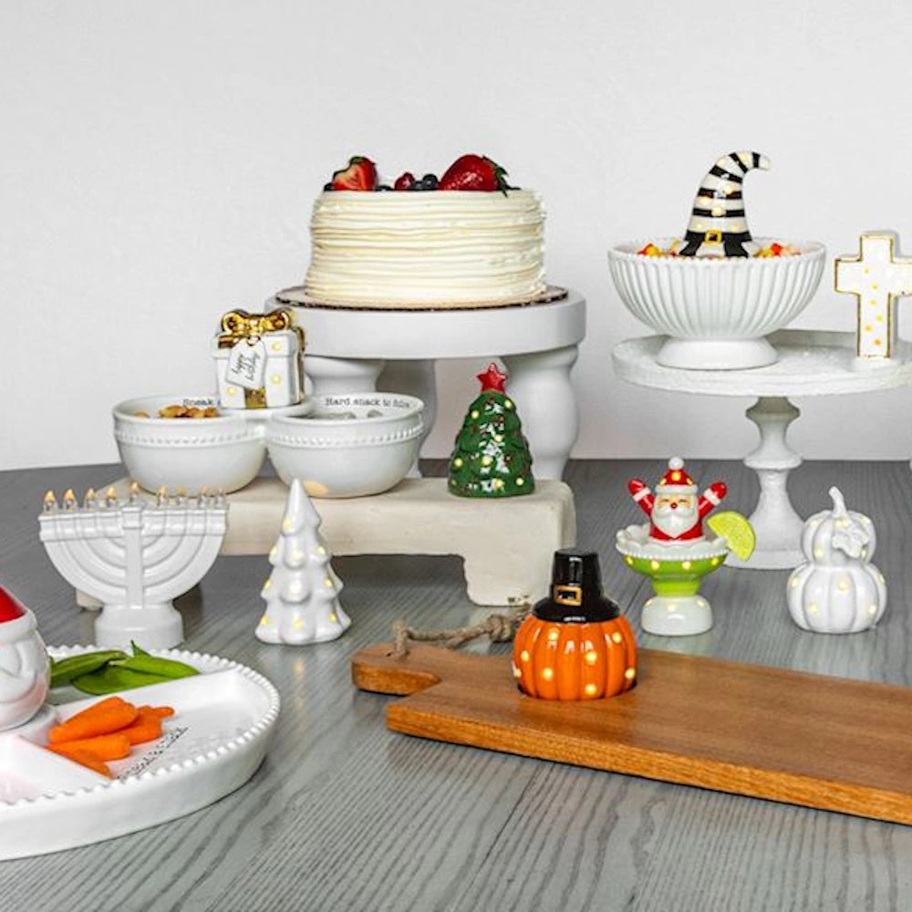 Festive holiday table display featuring light-up sitters, white ceramic serving dishes, and a cake.