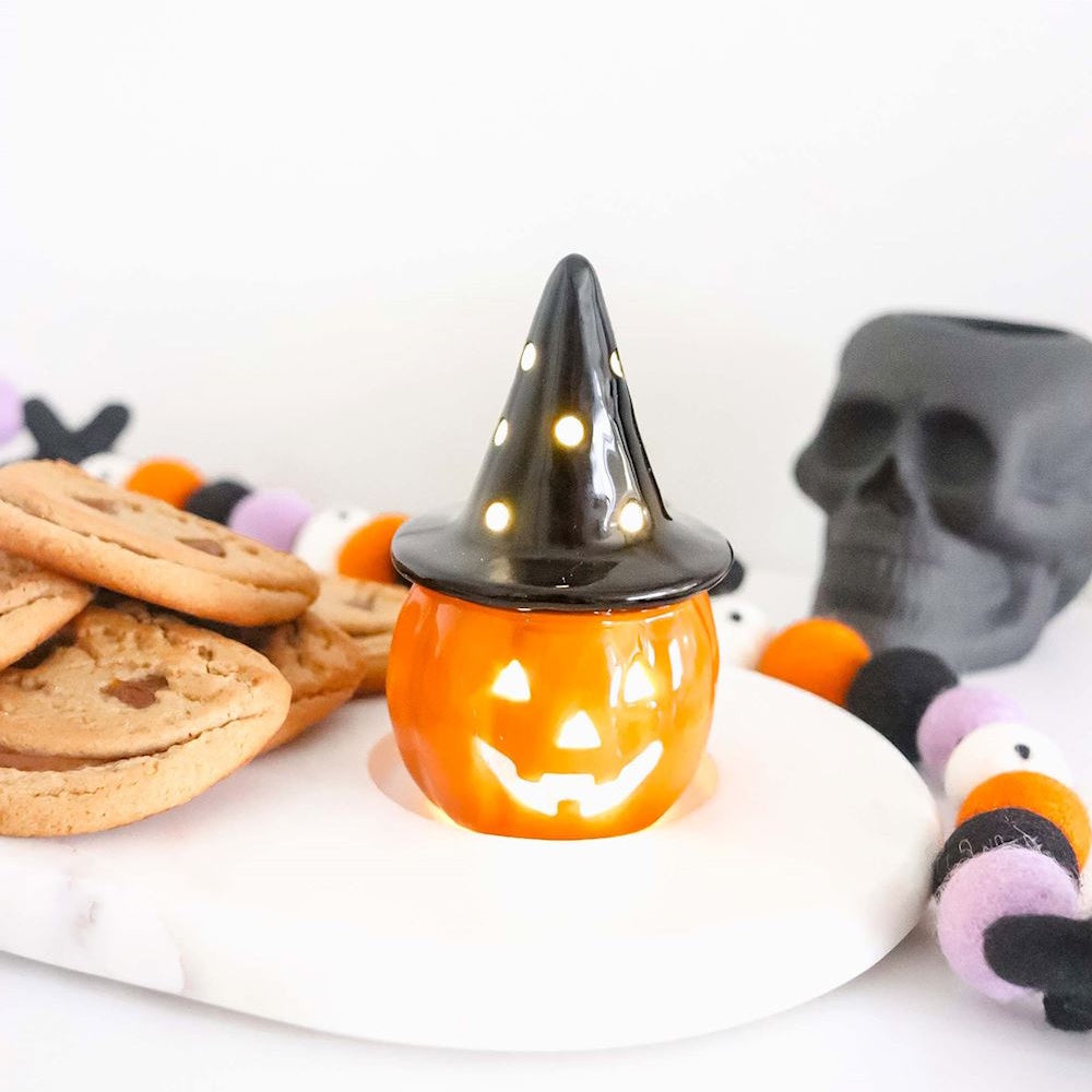 Light-up ceramic jack-o'-lantern with a witch hat on a Halloween treat table.