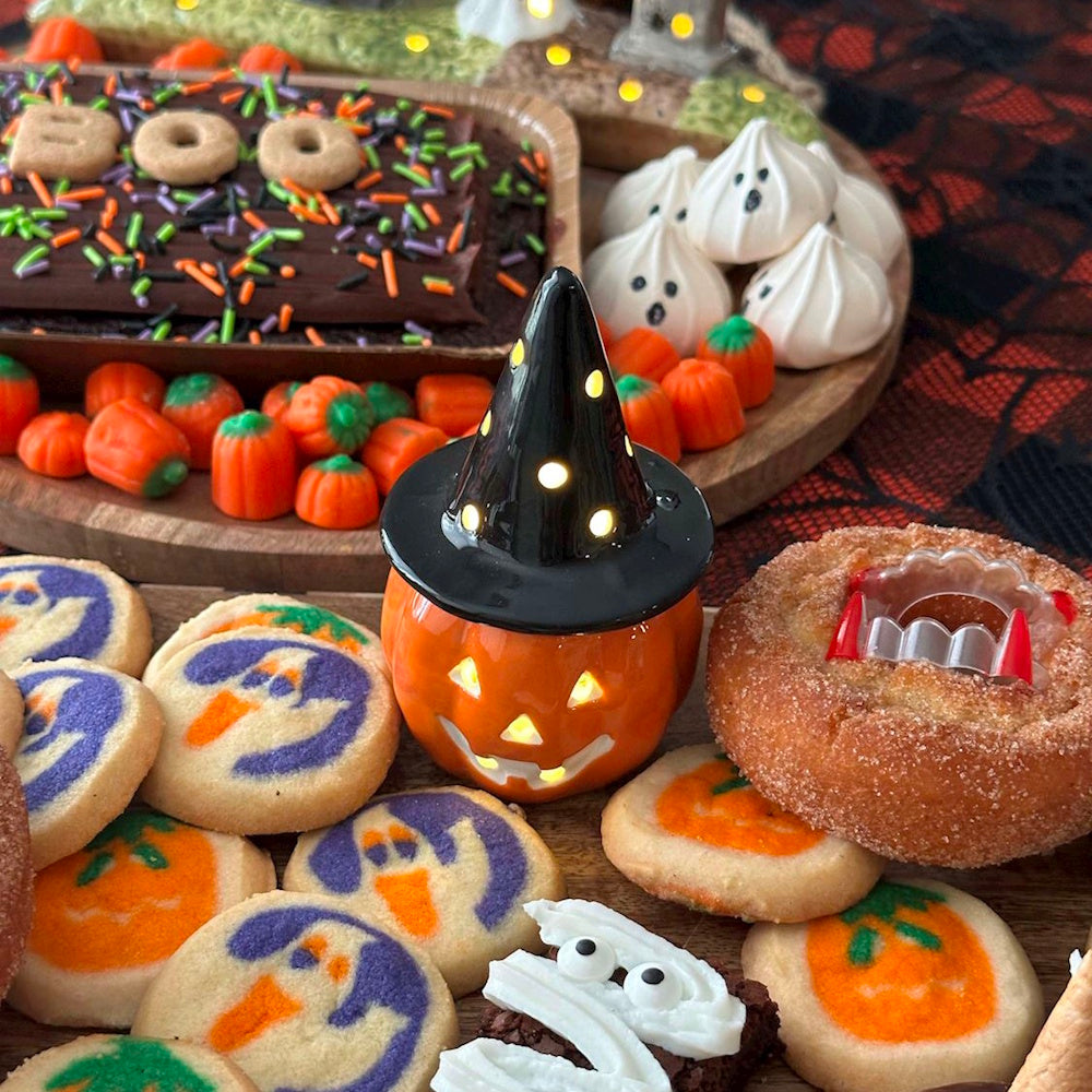 Halloween dessert spread with a light-up witch jack-o'-lantern decoration and spooky ghost cookies.