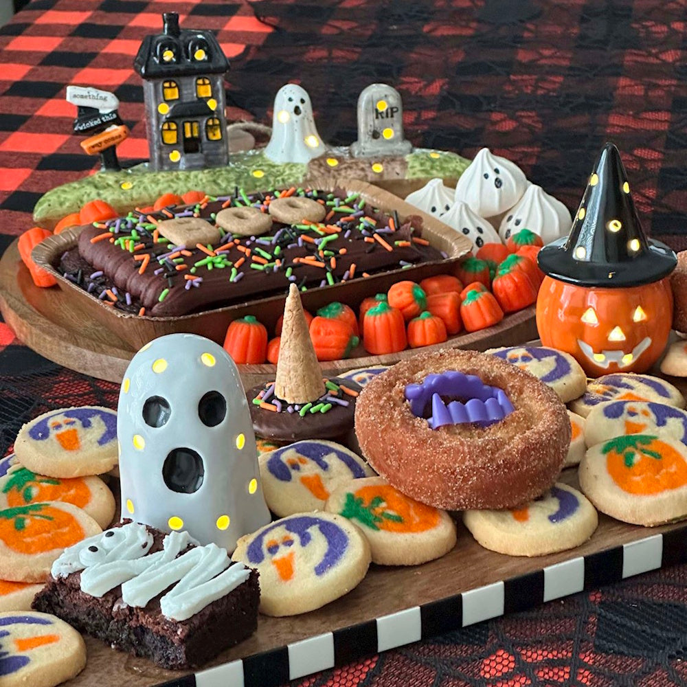 Halloween party dessert board with ghost and pumpkin cookies, brownies, donuts, and light-up decorations.