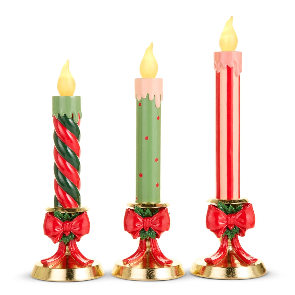 Front view of three colorful LED taper candles on gold base stands with red bows.