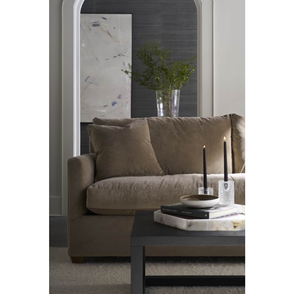 Modern taupe fabric sofa in a styled living room with a black coffee table and lit candles.