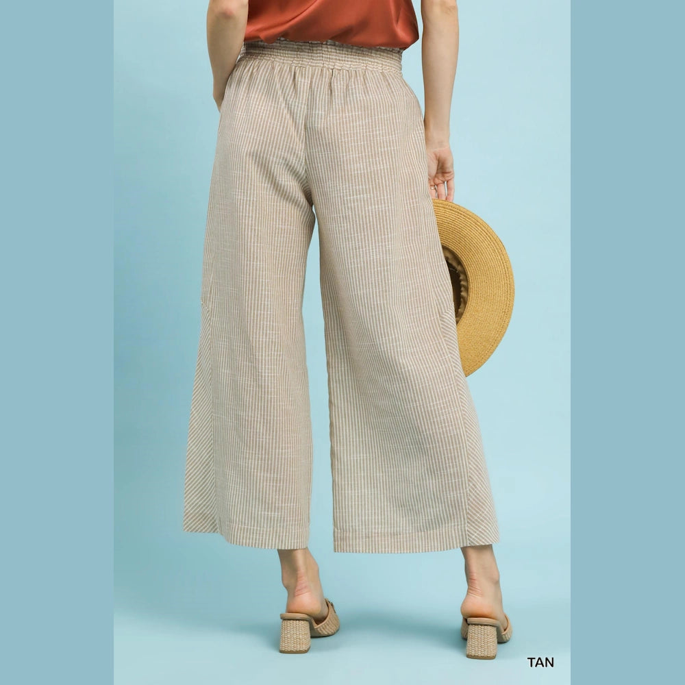 Tan and white vertical striped wide-leg linen pants with an elastic waistband, styled with a straw hat and heels.