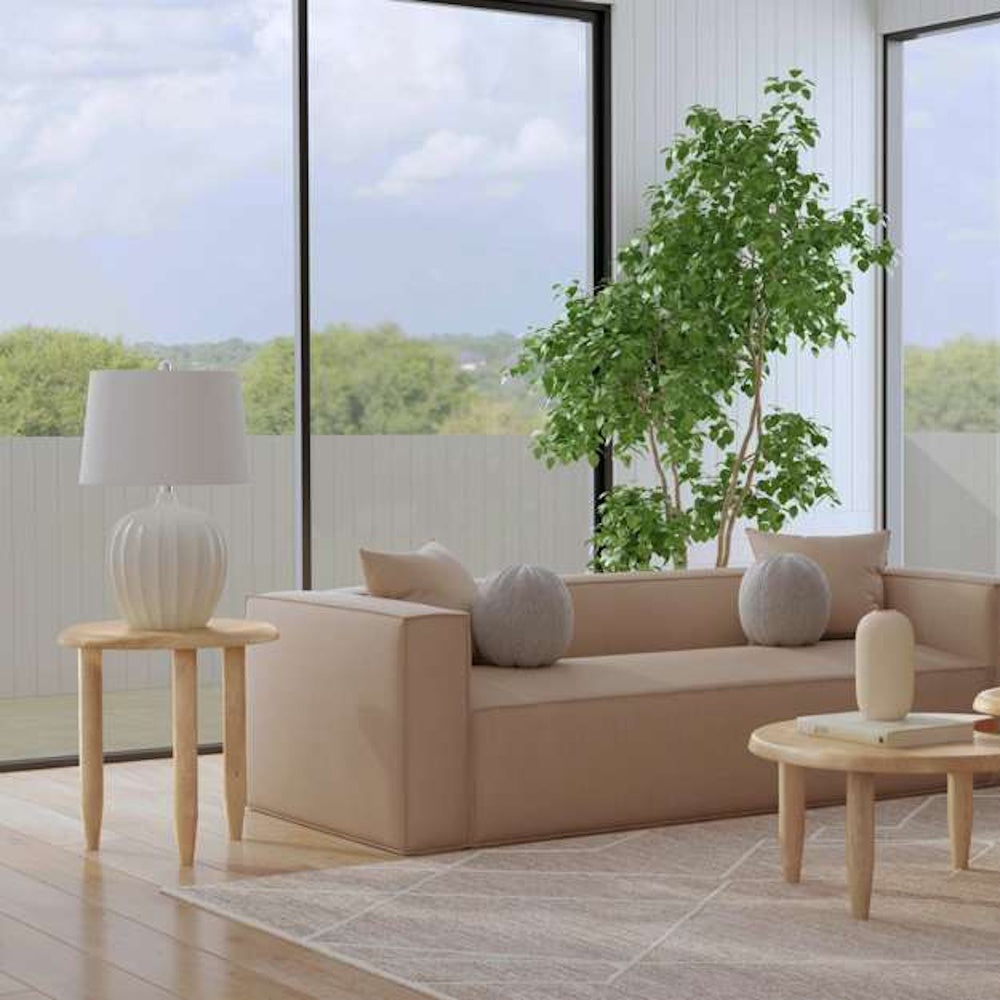 Modern minimalist living room with beige sofa, wooden side tables, and large indoor plant by a window.