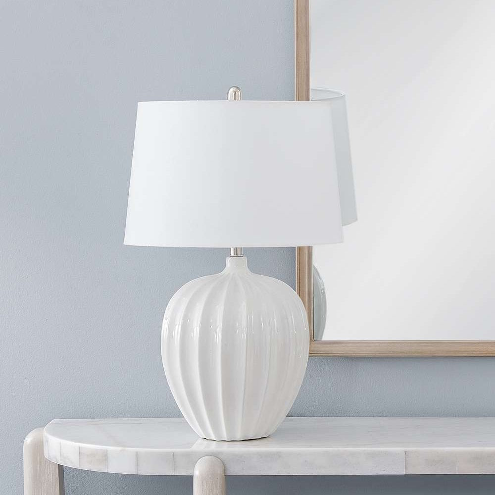 Modern white ribbed ceramic table lamp with a white drum shade on a marble console table.