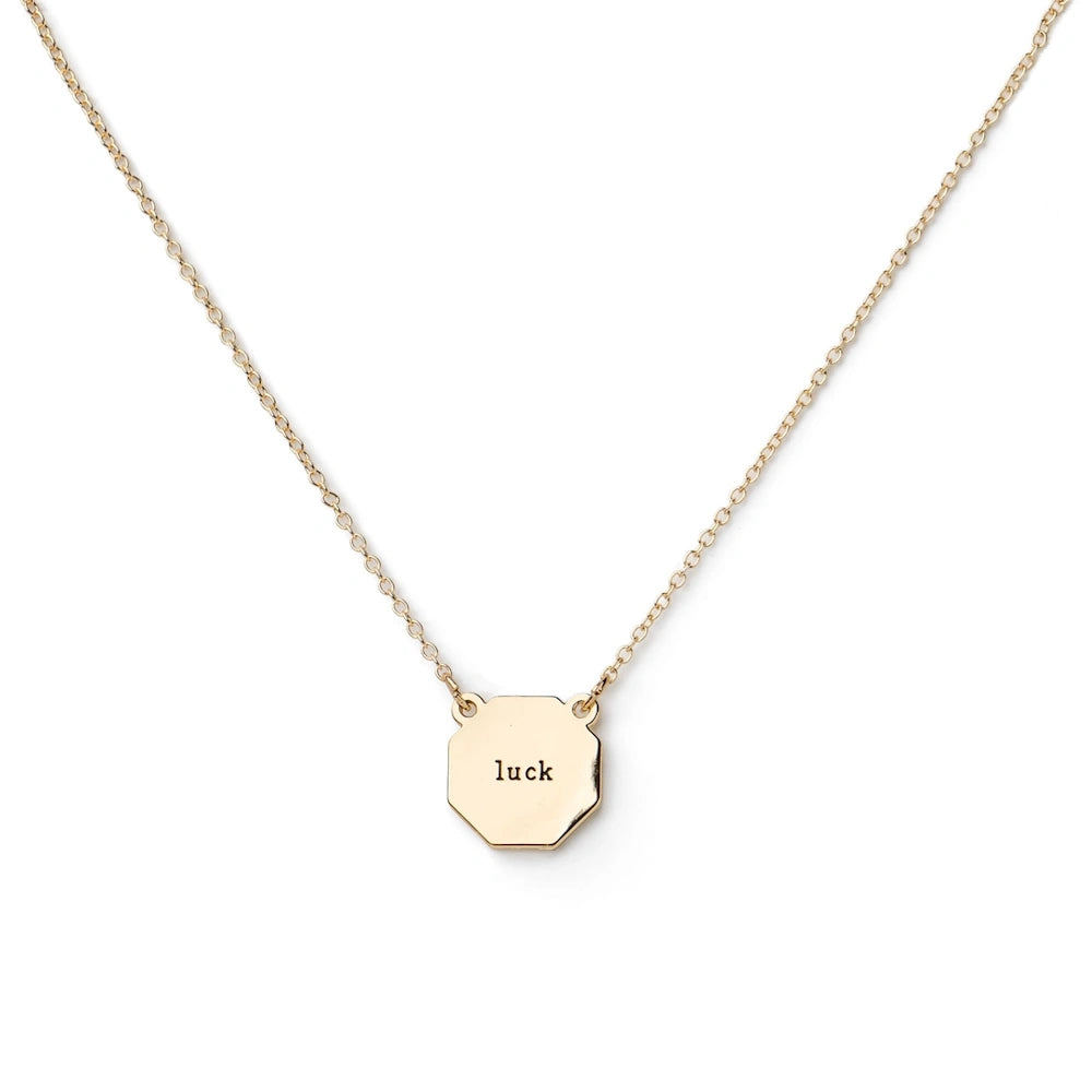 Gold necklace with a small hexagonal pendant engraved with the word "luck" on a white background.