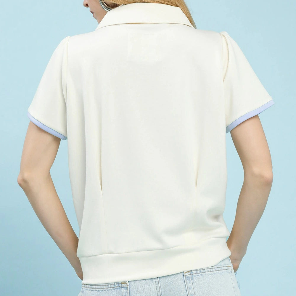 Back view of a cream short-sleeve knit polo with light blue trim on sleeves, paired with light-wash jeans.