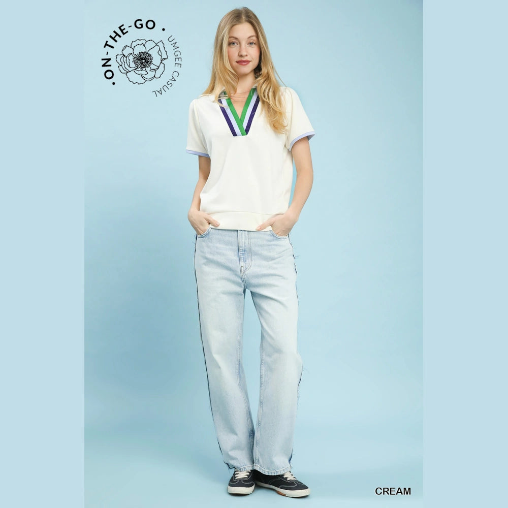 Woman in a cream V-neck short-sleeve top with green and blue trim, paired with light-wash jeans against a blue background.
