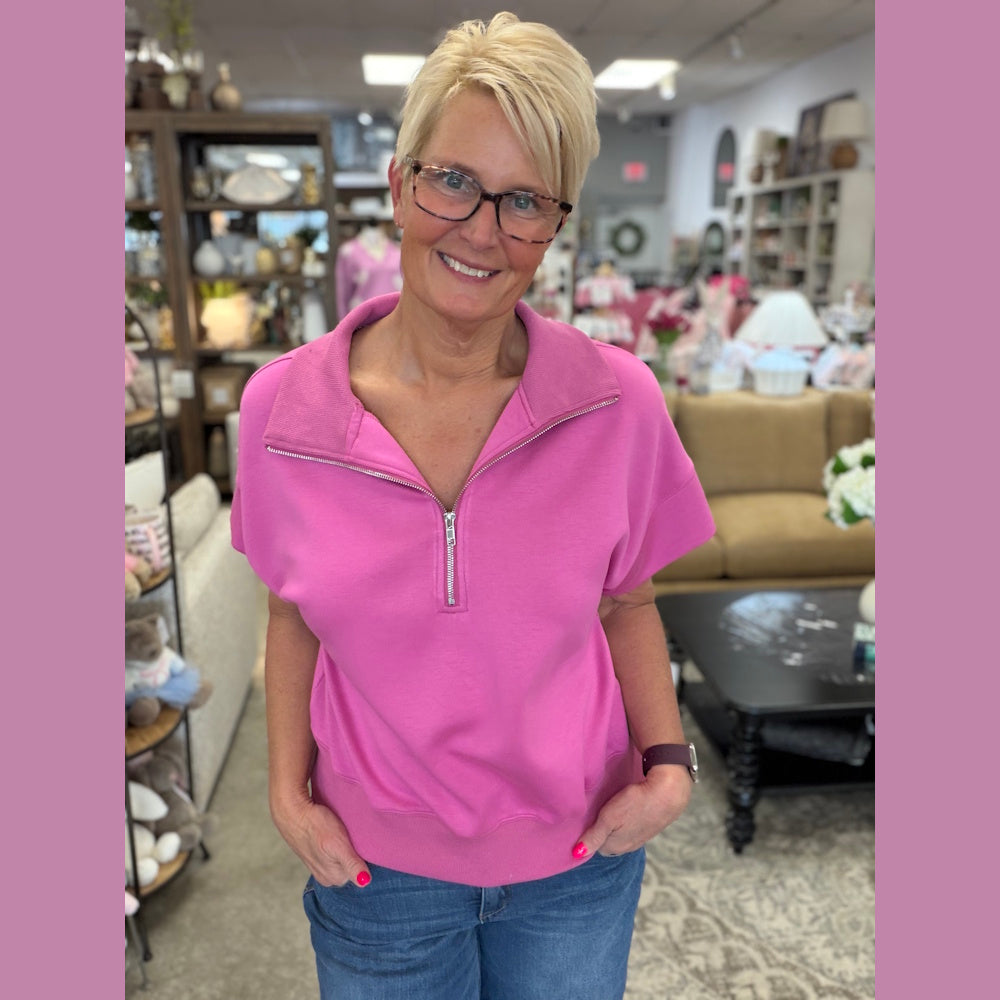 Woman in a peony pink LuxeKnit relaxed half-zip short sleeve pullover sweater and jeans in a boutique setting.