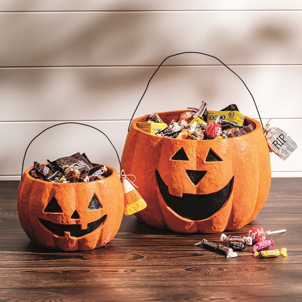 Two jack-o'-lantern trick-or-treat buckets filled with Halloween candy on a wooden table.