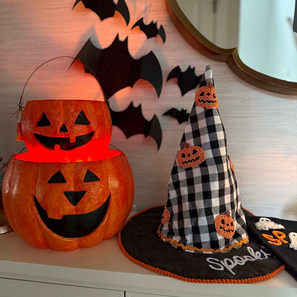 Stacked Halloween Jack-o'-lantern buckets next to a plaid witch hat and wall bat decor.