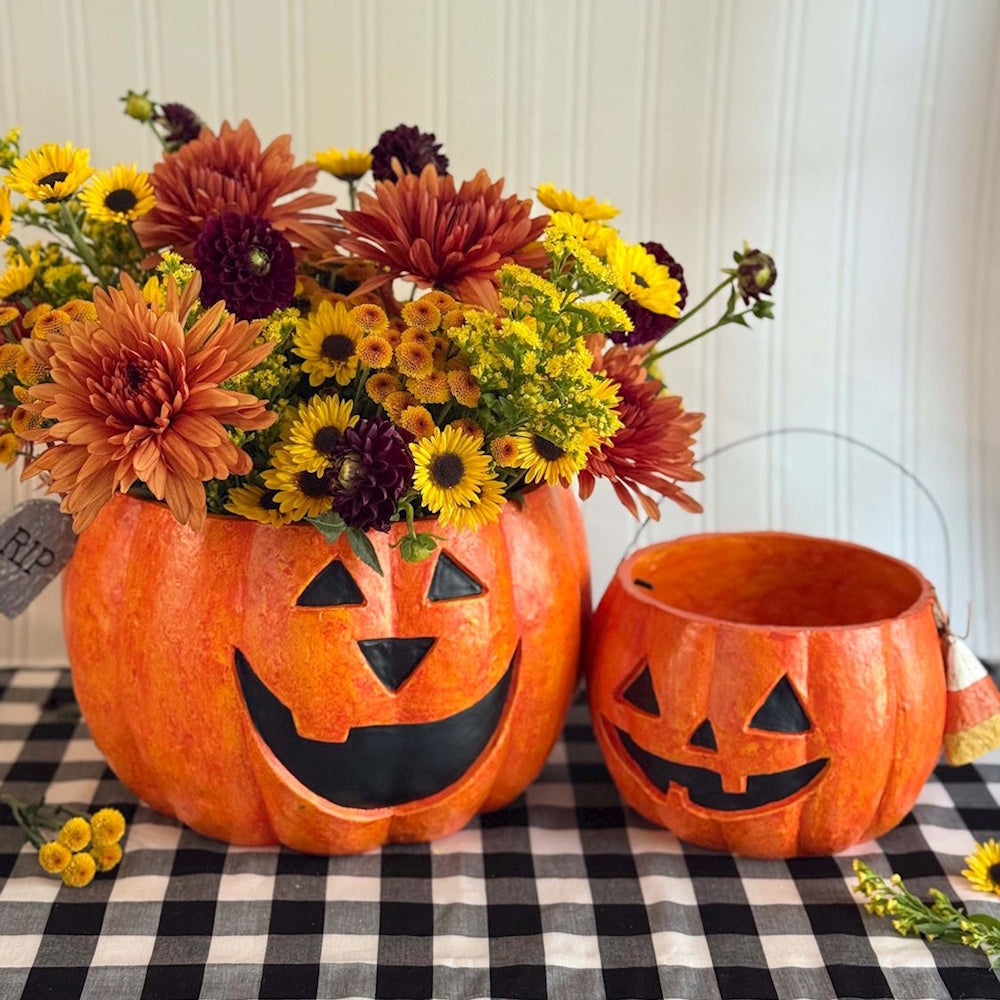 Pumpkin jack-o-lantern buckets filled with fall flowers for Halloween decor.
