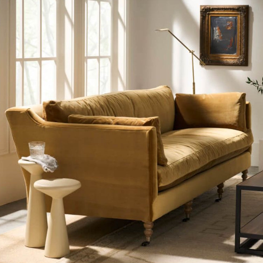 Mid-century modern mustard yellow velvet sofa with a nested side table in a bright, sun-drenched living room.