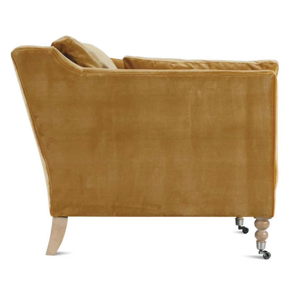 Mustard gold velvet armchair side profile, featuring elegant turned front legs with casters and a splayed rear leg.
