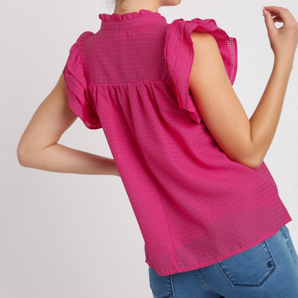 Back view of a person wearing a magenta, sleeveless top with tiered ruffle shoulders and a ruffled collar.