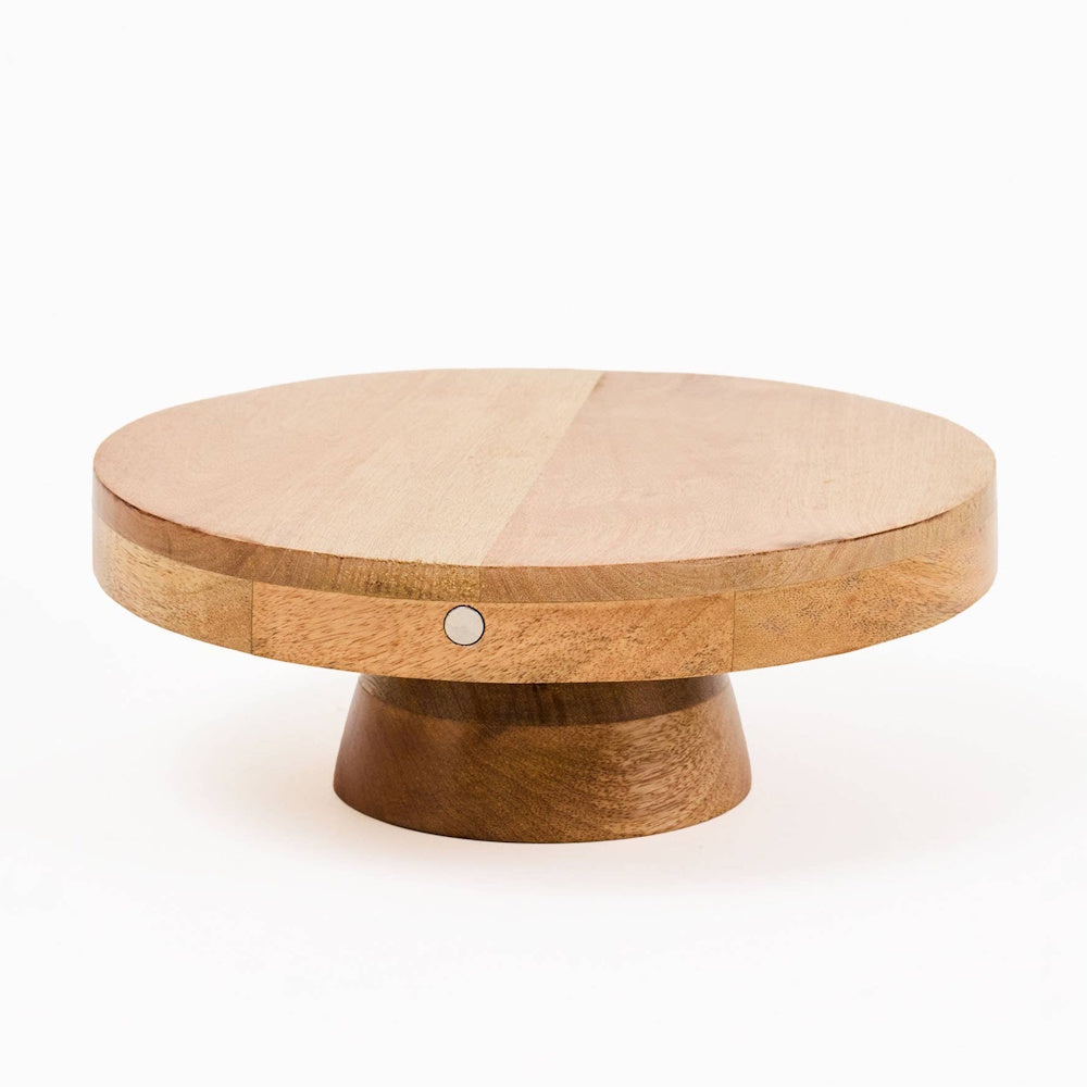 Round wooden cake stand with a low pedestal base and a small circular metal accent on the edge.