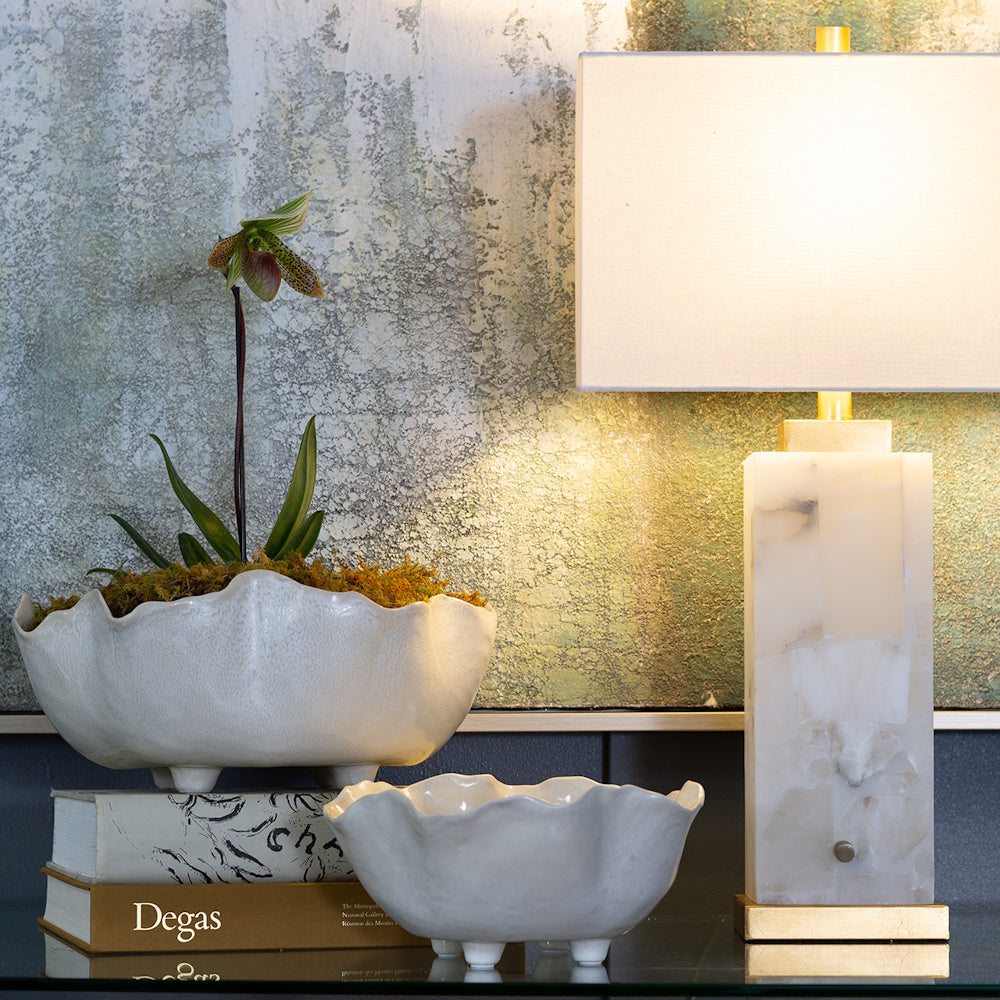 Two Magnus white ceramic scalloped bowls with feet on a desk next to an alabaster lamp and Degas art books.