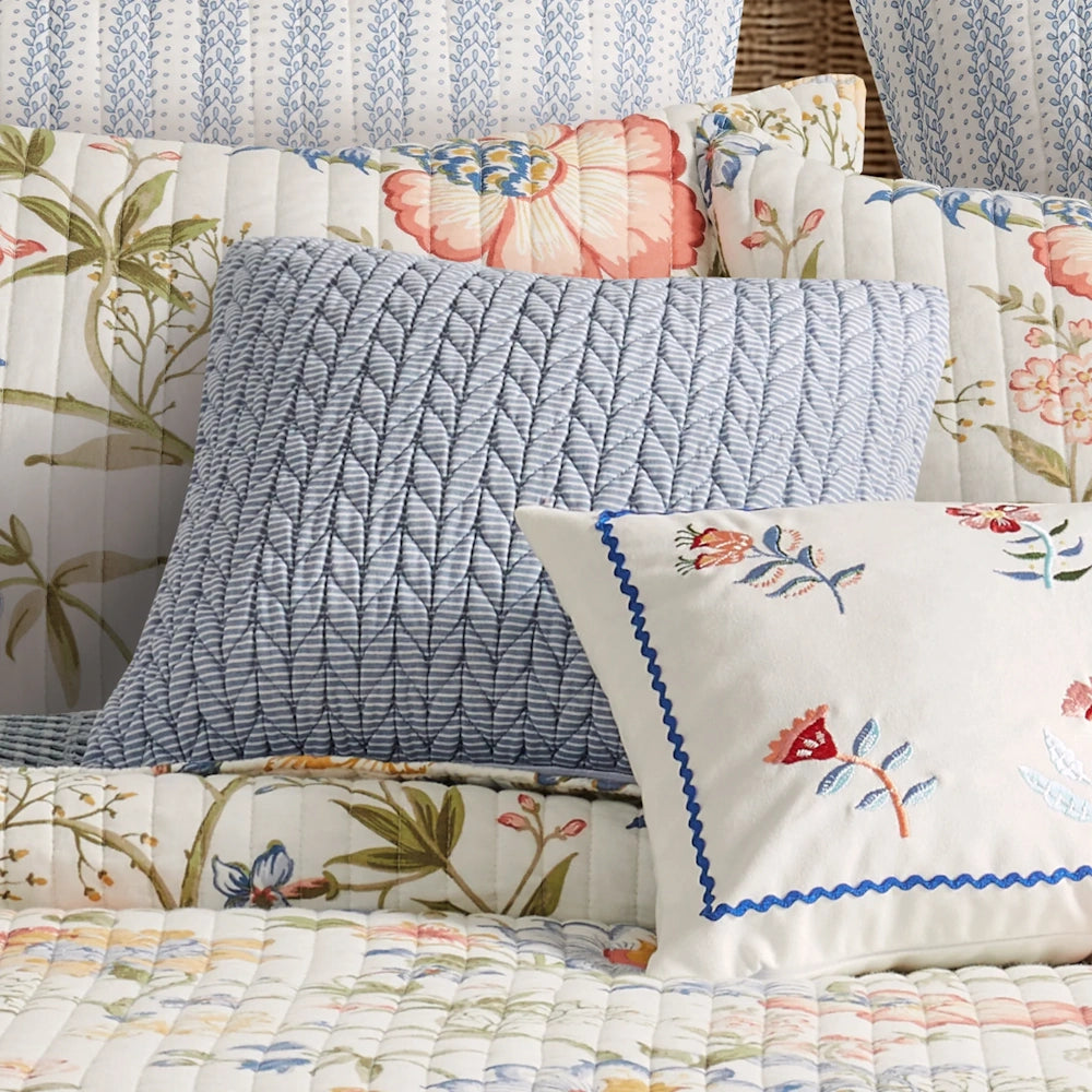 Close-up of a blue textured accent pillow and floral decorative pillows arranged on bedding.