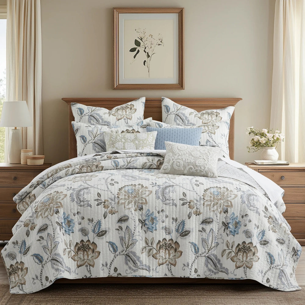 Bed set with neutral blue floral quilt, matching shams, decorative pillows, and framed botanical art above.