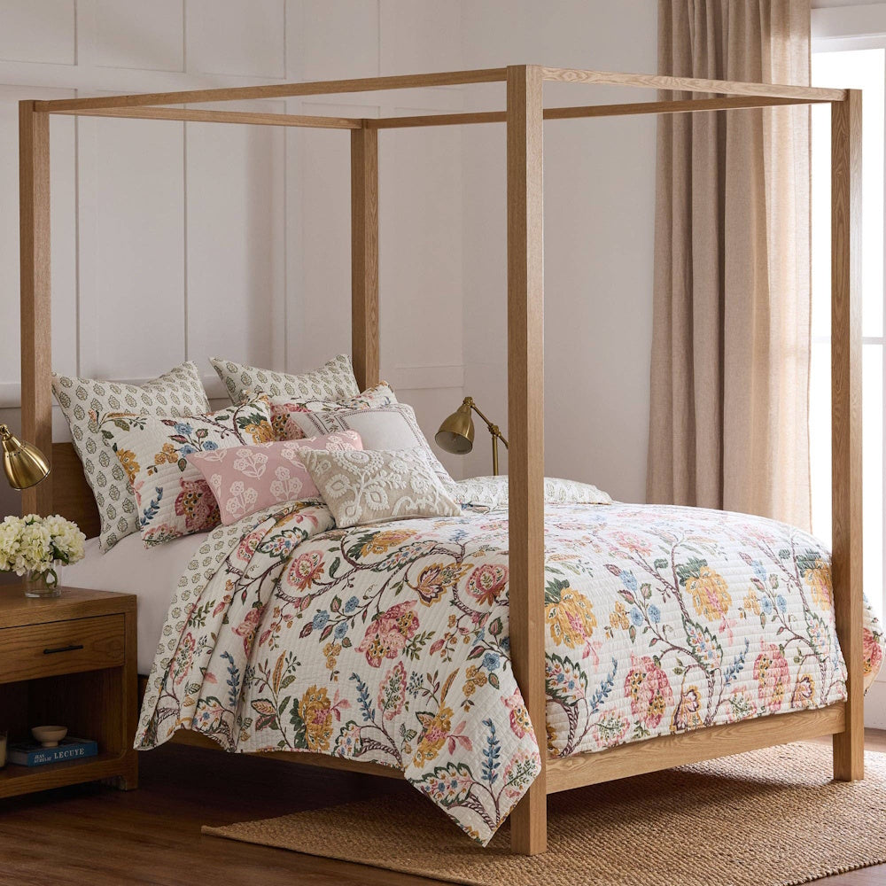 Floral trail quilt set on a wood canopy bed with decorative pillows.