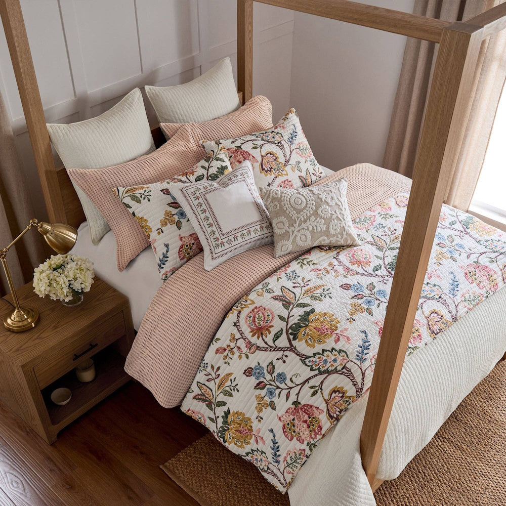 Elegant floral quilt set on a wooden canopy bed with matching patterned pillows and a pink waffle knit throw.