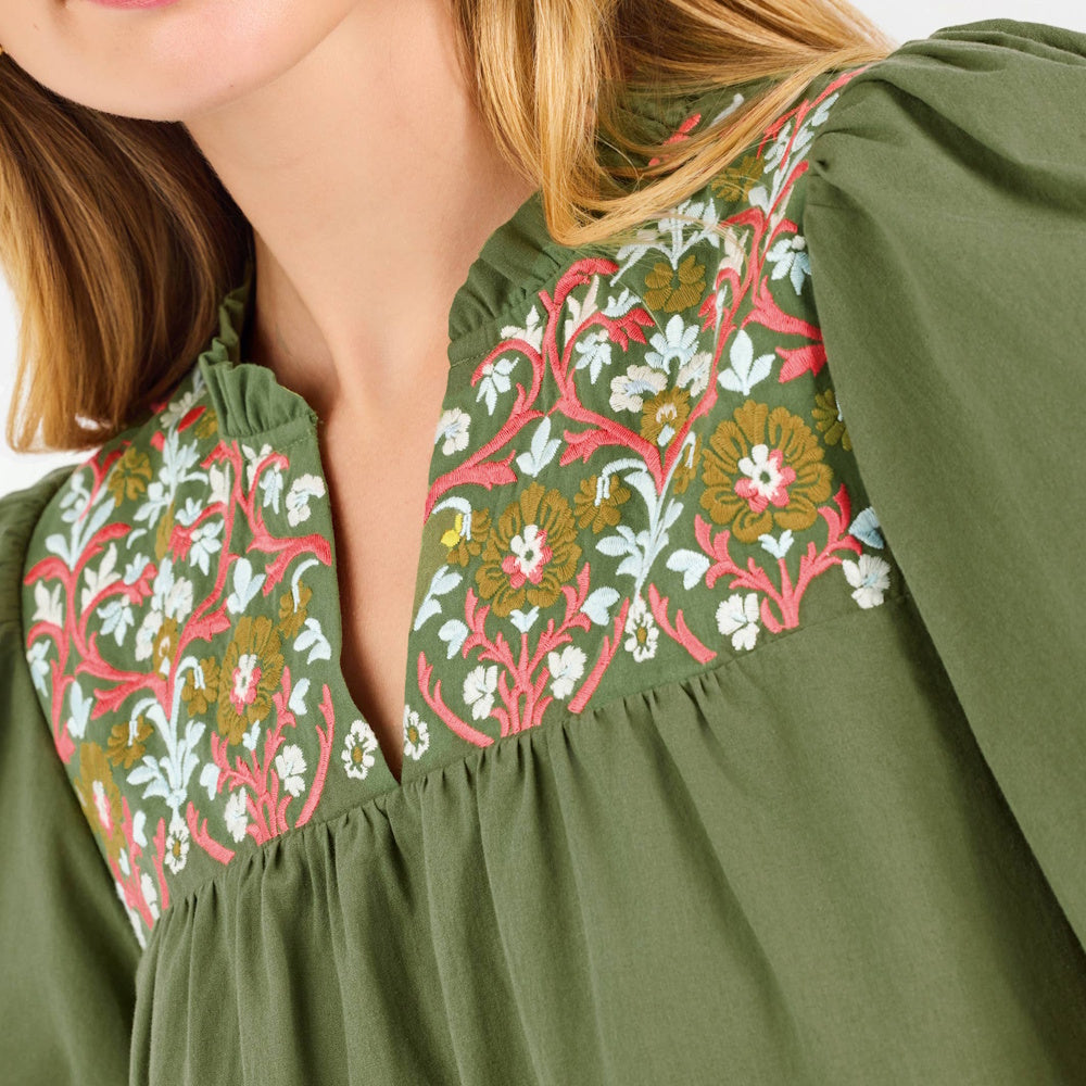 Close-up of an olive green top with pink and white floral embroidery along the split neckline.