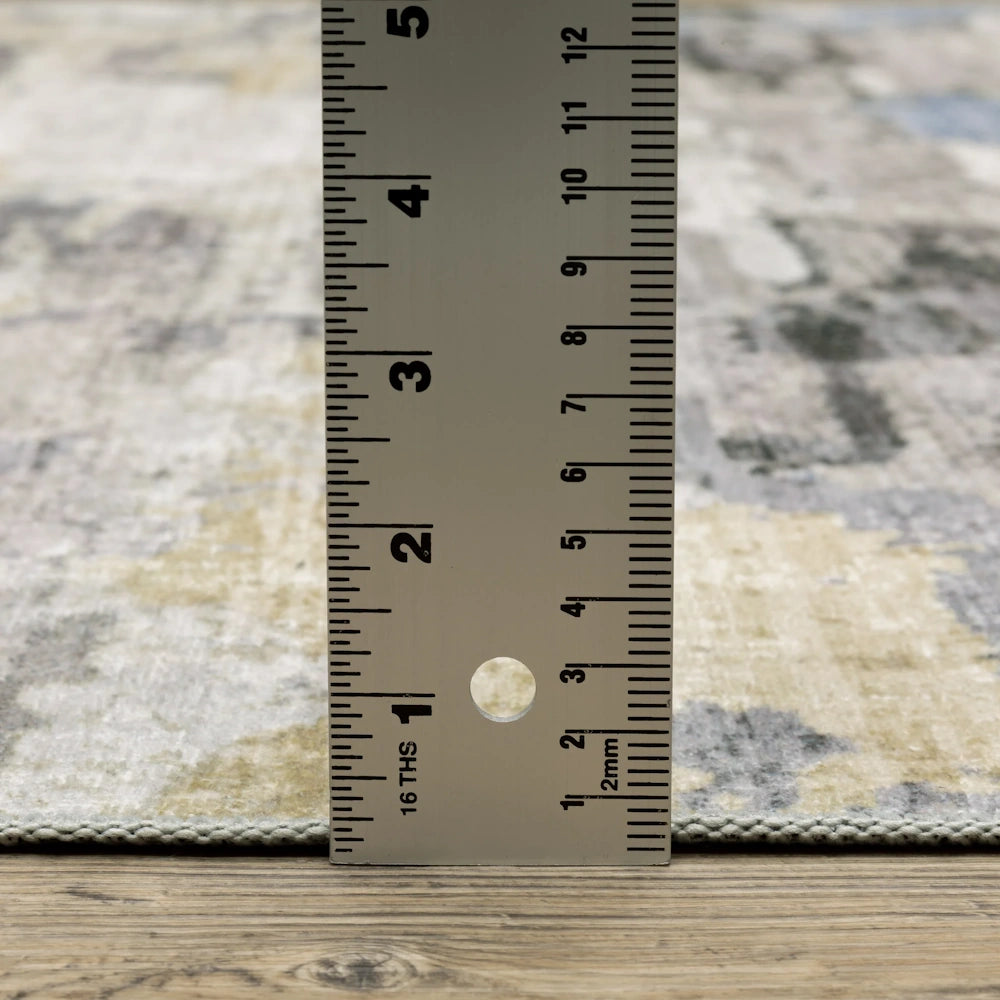 A ruler measures the thickness of a textured grey and beige rug, showing a pile height of under 0.25 inches.