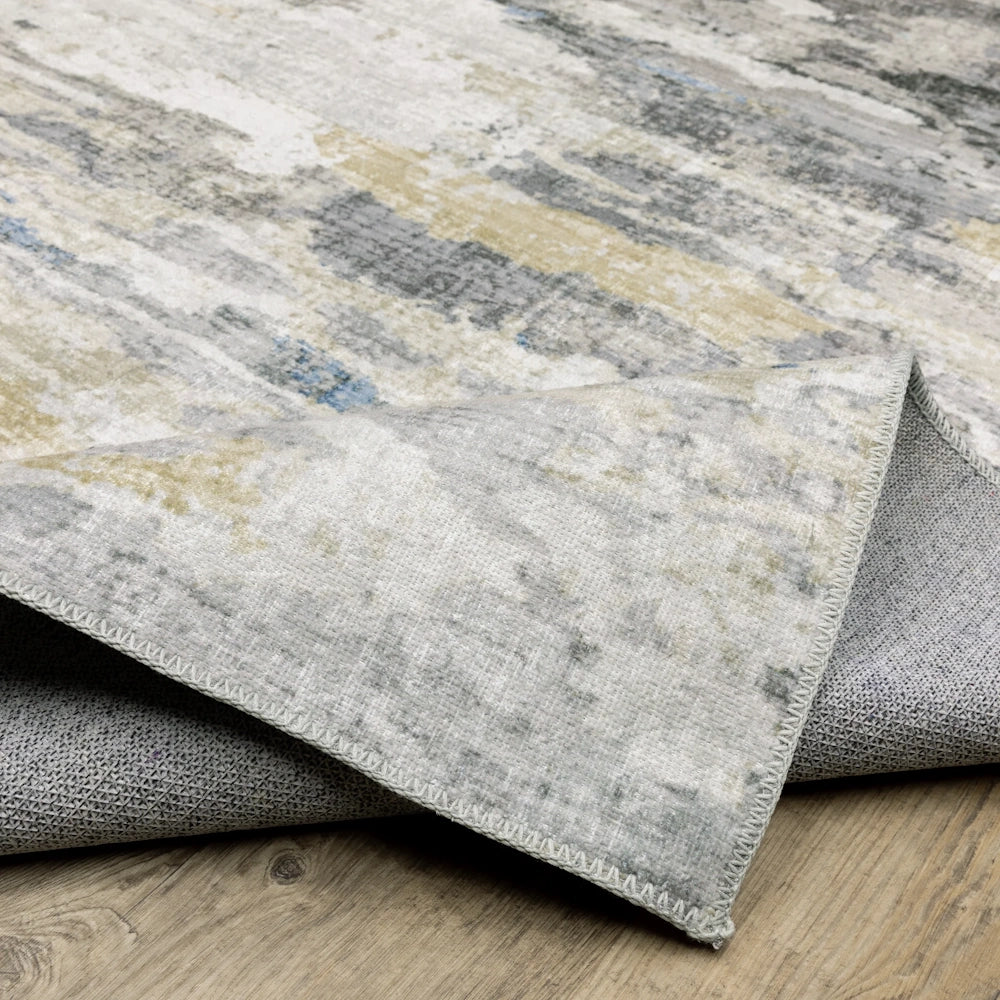 A folded corner of an abstract grey, beige, and blue rug, showing its non-slip textured backing.