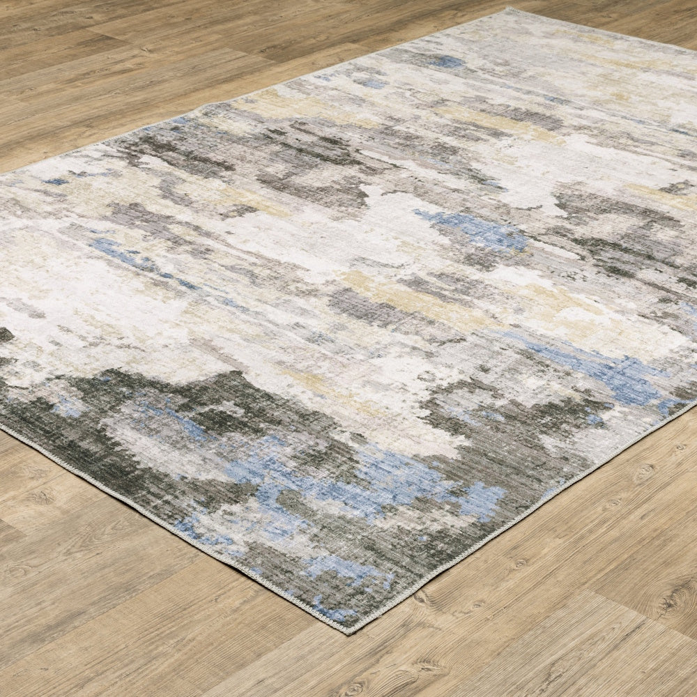 Side-angle view of an abstract area rug with a distressed blue, gray, and cream pattern on wood flooring.