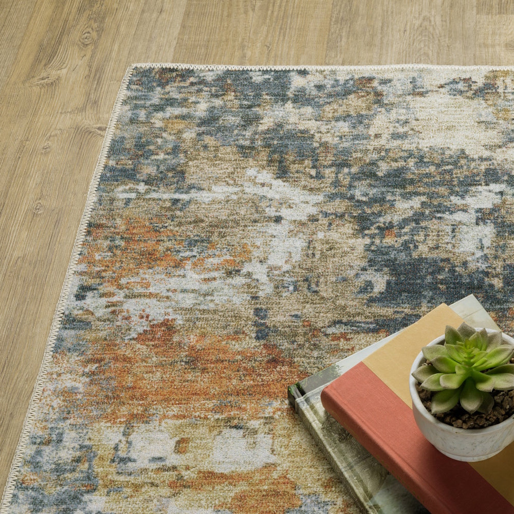 An abstract orange, blue, and cream rug on wood floors, partially styled with books and a small potted succulent.