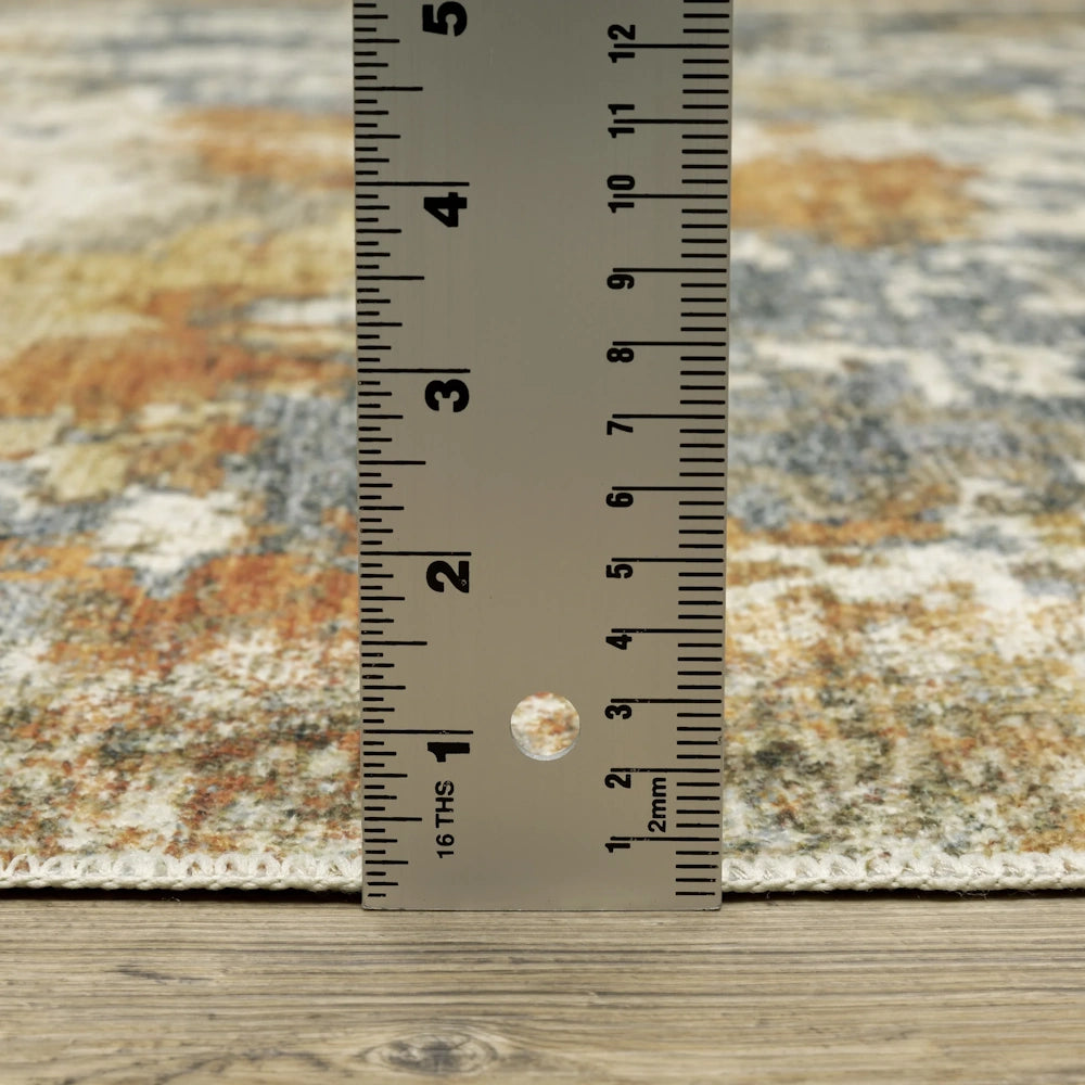 A metal ruler measuring the pile height of a patterned area rug with blue, cream, and orange tones.