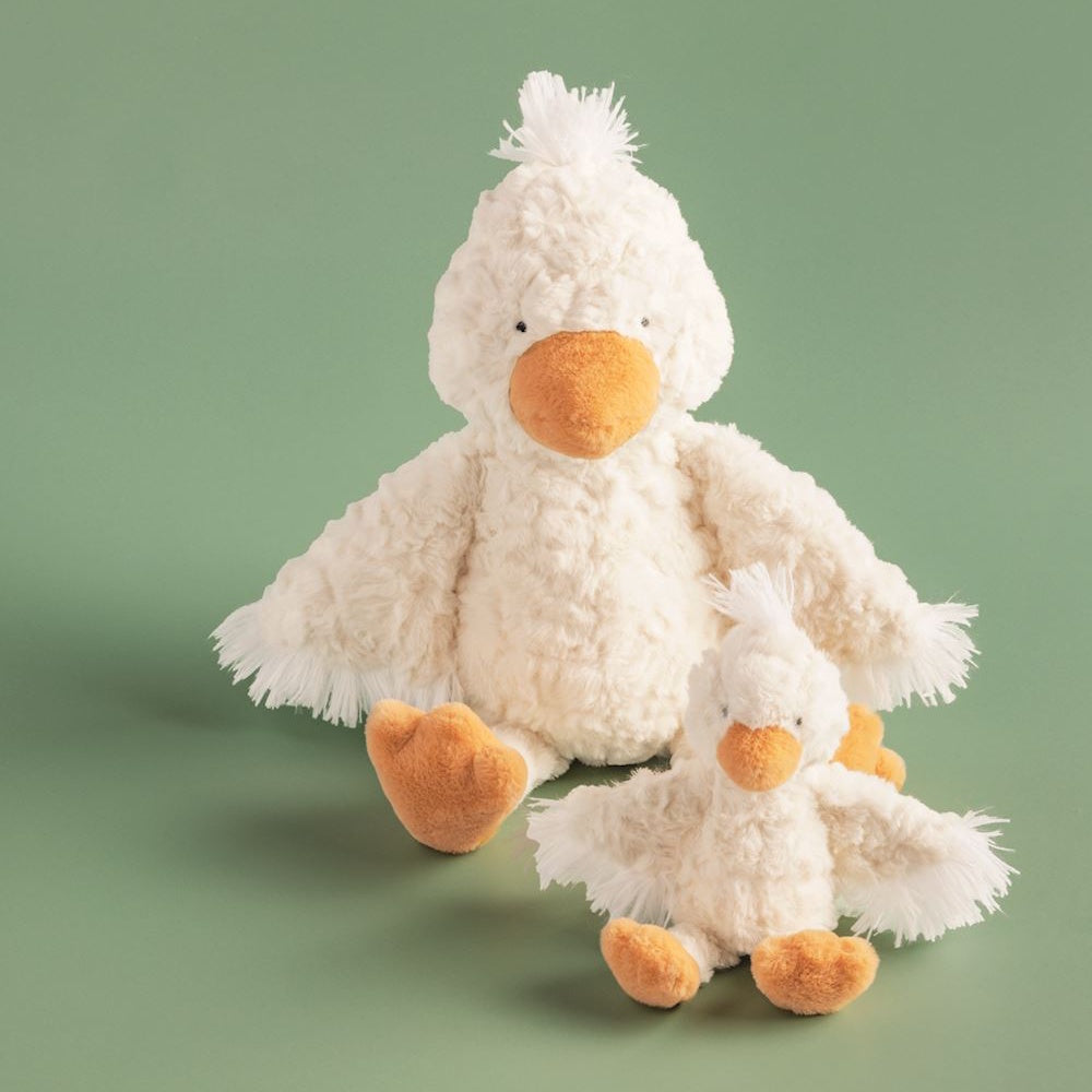 Mama and baby white duck plush toys with outstretched wings and orange beaks on a green background.