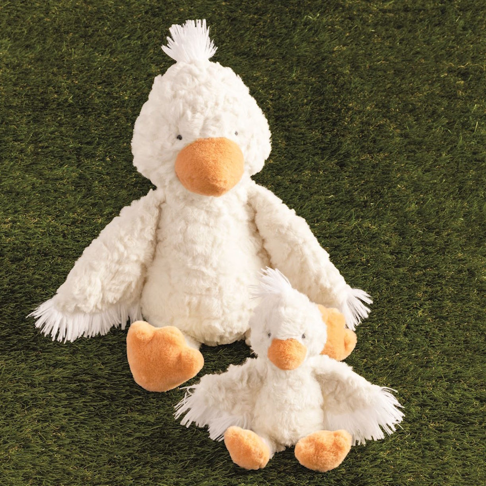 Mama and baby white duck plush toys with orange beaks and feet sitting on green grass.