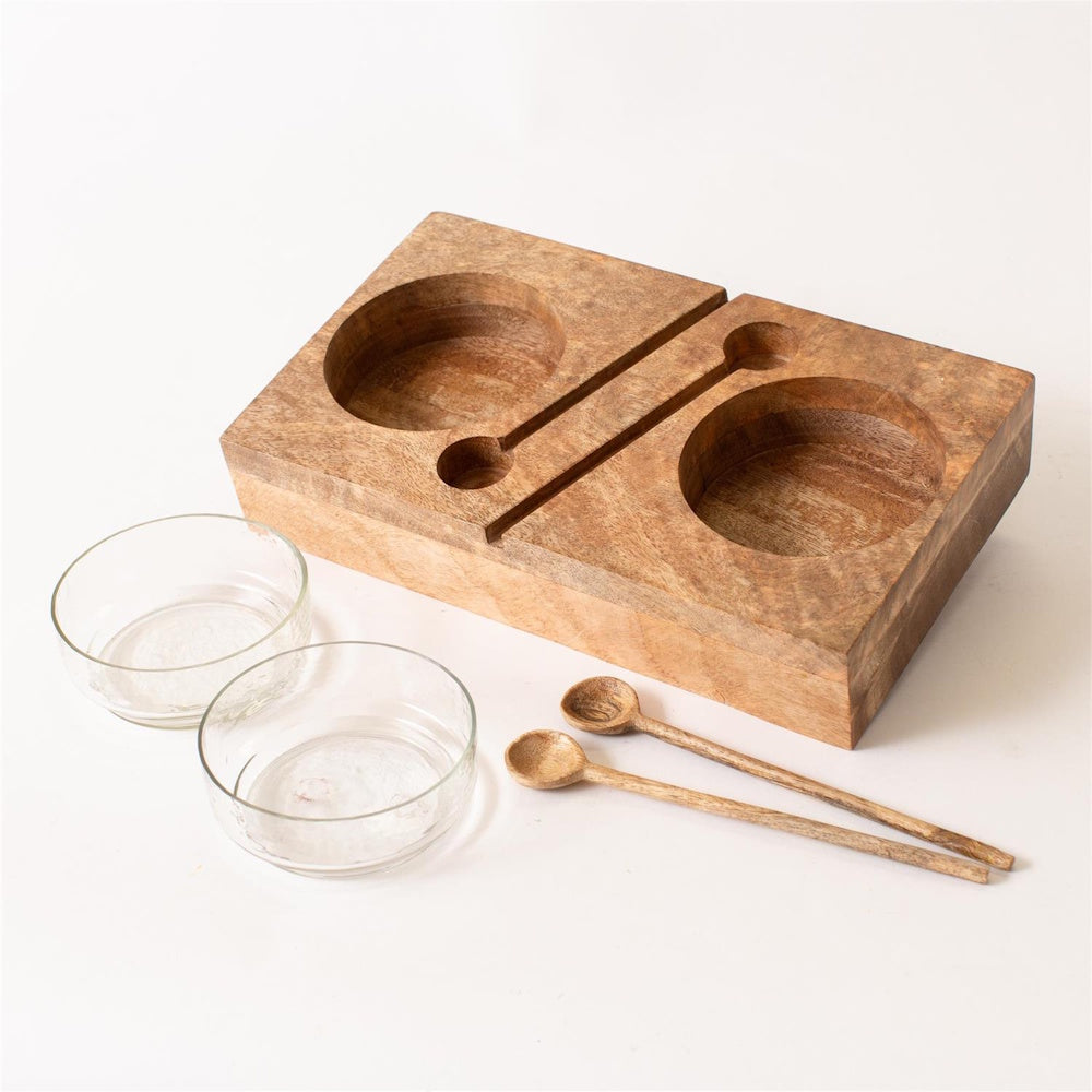 Wooden serving tray with recessed cutouts, two clear glass bowls, and two wooden spoons.