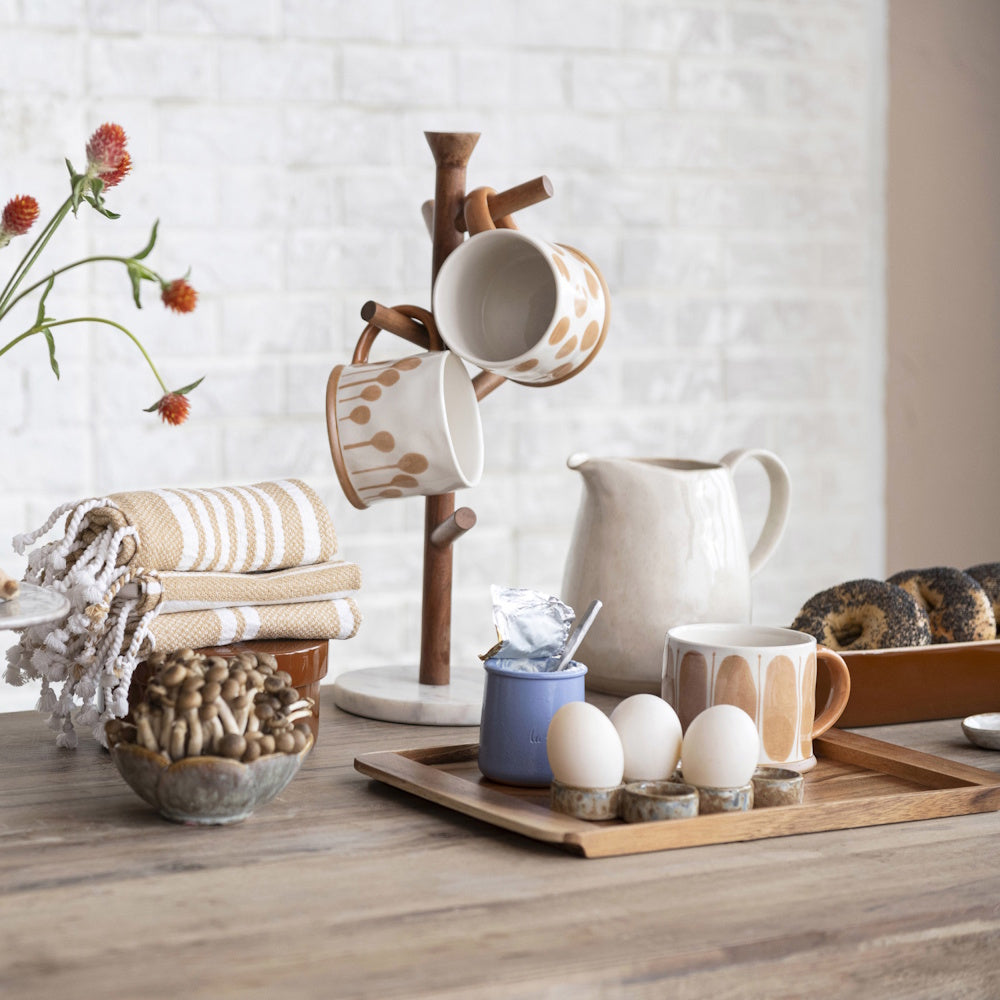 Mango wood and marble mug tree on a wooden table with patterned mugs, eggs, bagels, and neutral kitchen decor.