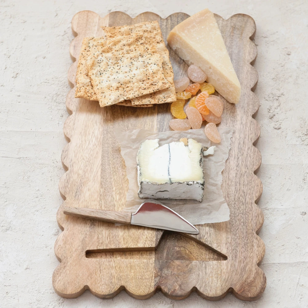 Wooden scalloped cheese board with assorted cheeses, crackers, and a spreader knife.