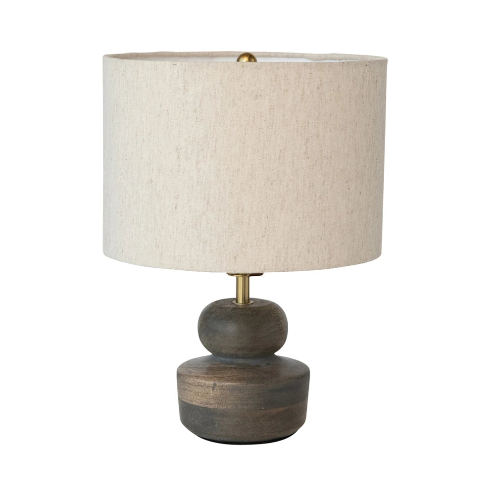 A table lamp featuring a dark carved wooden base and a cylindrical cream linen shade on a white background.